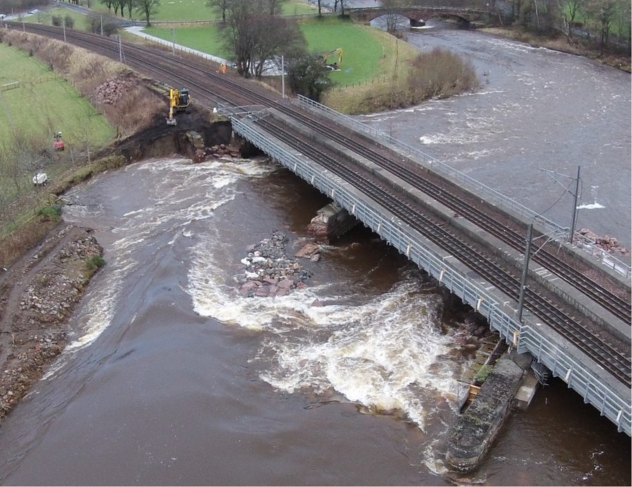 A railway bridge over a river in flood. The bridge has suffered structural failures of its pier supports due to flood water scour